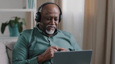 Portre olgun erkek kulaklık öğretmeni online danışman işletme eğitmeni kulaklıkla konuşan yaşlı Afro-Amerikan iş adamı konuşan dizüstü bilgisayarlı web kamerası web sitesi yönetmeni. Yaşlı adam uzaktan ders veriyor.