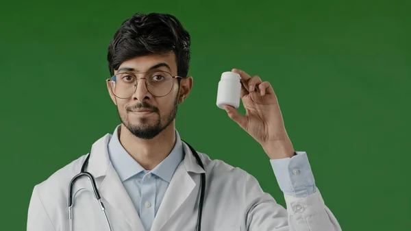 緑の背景の上に立って医療コートのインドの男性若い医師の顧問は アレルギー医療からの治療のための鎮痛薬ビタミン錠薬とカメラボトルでお勧めします — ストック写真