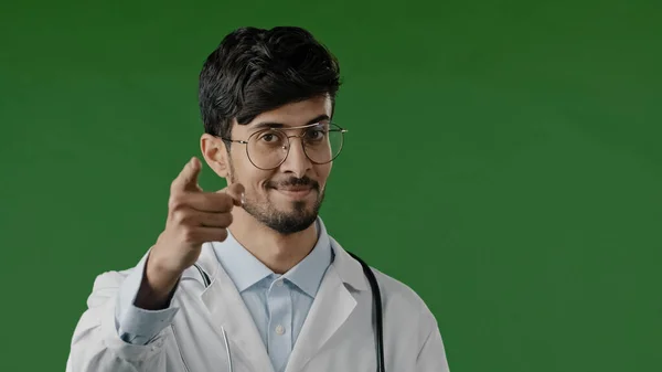 Arabic doctor man smiling hispanic male medical worker raises index finger warns you to be attentive disbelief looks at camera express ironic emotion stands over green background shows caution gesture