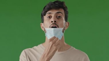 Yorgun Arap esmer adam, Hintli İspanyol adam yeşil stüdyoda tek başına duruyor. Solunum maskesi çıkarıyor, temiz hava alamıyor, nefes alamıyor salgın sırasında derin bir nefes alıyor.
