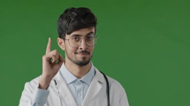 Arap doktor, gülümseyen İspanyol erkek doktor işaret parmağını kaldırır. Dikkatli olun. İnançsız olun, kameraya bakın.