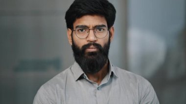 Ciddi anlamda yakışıklı, Arap kökenli, gözlüklü, gözlüklü, gömlek giyen, kapalı mekanlarda poz veren, mutsuz, esmer, yetişkin, Hintli iş adamı bir Latin erkeğin portresi.