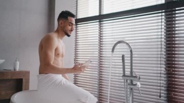 Sabah banyosu, Arap Hintli çıplak sakallı, banyo havlusuyla banyoda oturmuş duş jeli, doğal erkek kozmetik sabah temizliği prosedürünü izliyor.
