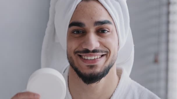 阿拉伯裔印度男子 头戴毛巾 头戴面霜罐 笑着看着相机 推荐浴室里的天然男性化妆品宣传面部保湿治疗水合 — 图库视频影像