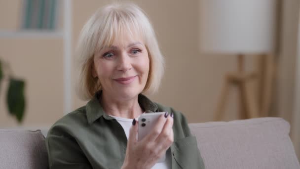 閉じるショックを受けたスマートフォンで自宅で高齢者の50年代の女性は素晴らしいニュースを受信します — ストック動画