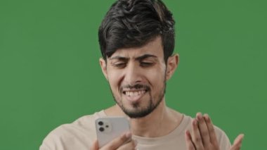 Stresli Arap genç adam yeşil arka planda akıllı telefondan konuşuyor. Cep telefonuyla kavga ediyor. Kötü kablosuz bağlantı, uzaktan kumandalı anlaşmazlık.