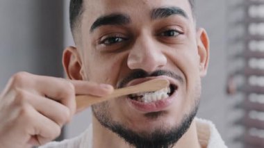 Aşırı yakın plan, sakallı, yetişkin, yakışıklı, Hintli, İspanyol bir adam banyoda dişlerini fırçalıyor. Portre hipster Arap etnik kökenli adam ağız hijyenik günlük diş tedavisi, diş bakımı yapıyor.