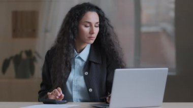 Konsantre kadın Arap iş kadını çoklu görev yapan muhasebeci maliyet dengesini hesaplar dizüstü bilgisayarı kullanır çevrimiçi ödeme e-ticaret eksiksiz mali rapor formları imza belgesi imzalar