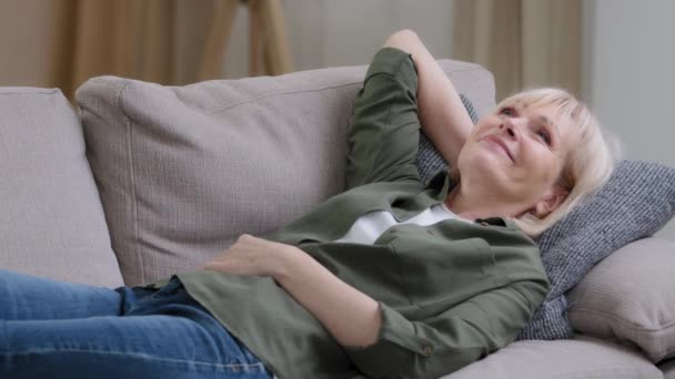 快乐悠闲的中年妇女沉思着睡在家里的沙发上享受着宁静的心情 困倦的懒散的老太婆梦躺在客厅里舒服的沙发上无忧无虑的放松 — 图库视频影像