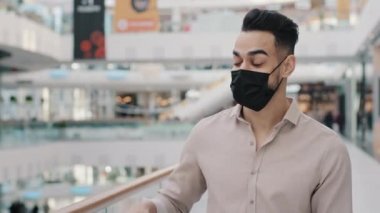 Maskeli Arap bir adam, tıbbi maskeli bir müşteri alışveriş merkezinde elinde alışveriş çantasıyla duruyor hediye paketlerine işaret ediyor indirimli indirimlerle neşe saçıyor başarılı alışverişler yapıyor.