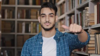Kütüphanede dikilip kameraya bakan mutlu genç bir çocuk başparmak işareti gösteren neşeli bir öğrenciye bakıyor. Bu, iyi bir eğitimden memnun kaldığının mükemmel bir göstergesidir.