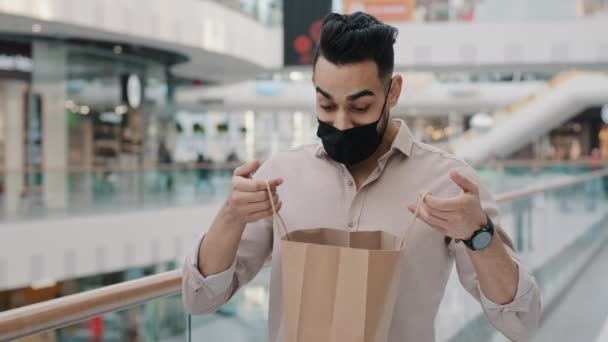 成功的富有的Arab印第安商人戴着医用黑脸面具30多岁的男人买方客户男人看着购物袋喜出望外购物打折销售表现出满意的姿态 — 图库视频影像