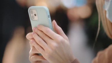Yakın plan kadın elleri akıllı telefon tutuyor. Medikal maskeli tanınmayan bir kız, akıllı telefondan doktor covid konsültasyonuyla mesajlaşarak cep telefonu uygulaması üzerinden ödeme yapıyor.