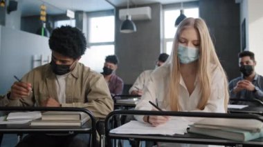 Tıp maskeli çeşitli öğrenciler derste oturup not defterinde ders notları dinlerler. Üniversite yüksek öğrenim kavramında okuyan genç öğrenciler.