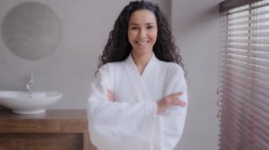 Genç, çekici İspanyol kadın banyoda bornoz giyiyor. Kendine güvenen kadın model, spa salonunda kollarını kavuşturup poz veriyor. Kozmetik ameliyattan memnun mutlu kız.