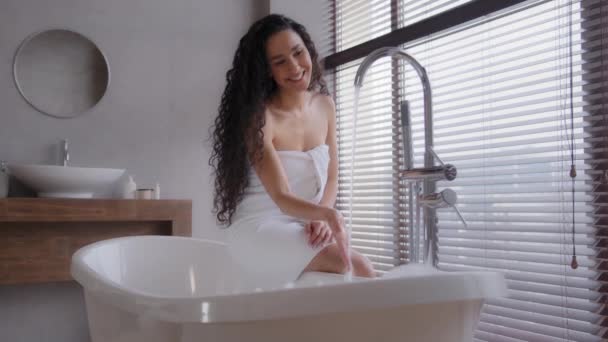 迷人的年轻快乐女人在热水下洗手漂亮的微笑的女孩坐在奢华的浴室里享受周末的免费身体护理让她感到轻松舒适 — 图库视频影像