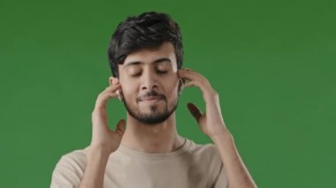 Stüdyo portresi yeşil arka plan mutlu kaygısız Arap adam İspanyol yakışıklı öğrenci kablosuz kulaklık takıyor yüksek sesli müzik kompozisyonu mp3 modern kulaklıklarda şarkı dansından keyif alıyor