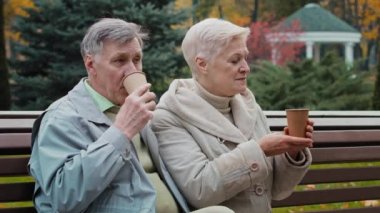Kaygısız yaşlı büyükanne ve büyükbaba dışarıda sıcak kahve içiyorlar yaşlı çift yaşlı erkek emekliler, büyük anne ve babalar bankta oturup dedikodu yapıyorlar sonbahar parkında birlikte rahatlıyorlar.