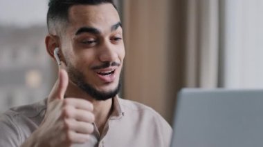 İnternetteki Arap erkek İspanyol erkek öğretmen web kamerası video konferansında kablosuz kulaklık takıyor. Anlaşmadan memnun olmuş el hareketi gösteriyor. İyi seçim alkışları.