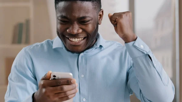 African young man surprised receive good message on cellphone win online bet rejoice passing mobile game level male american guy businessman feel shock yes gesture celebrate success internet victory