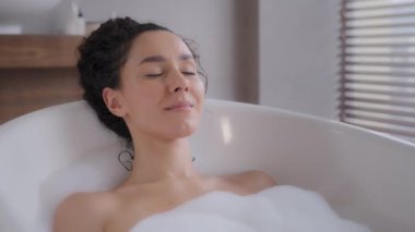 Close-up young attractive relaxed woman lying in hot foam bath with eyes closed resting relaxing in bathroom happy carefree pensive dreamy girl enjoying daily hygiene routine bathing washes bodycare