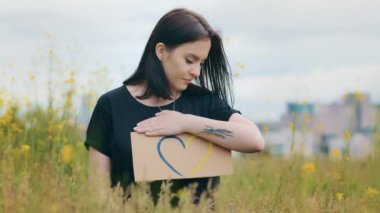 Attractive caucasian young teen girl woman patriot stand outside hold colorful cardboard drawing love shape heart sign in ukrainians colors blue yellow demonstrate national symbol of romantic feelings