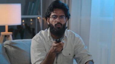 Akşam eğlencesi Arap Hintli, gözlüklü, karanlıkta sakallı, evinde yaşayan adam kanepe değiştirip kanalı değiştiriyor. İnternetten televizyon dizisi spor oyunu şampiyonası seyrediyor.