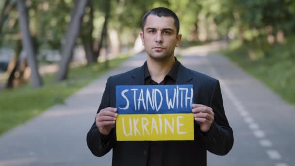 肖像悲しい深刻な男活動家愛国者男は 軍事紛争に対するウクライナの抗議と書かれた碑文スタンドと屋外ホールド段ボールスタンド反対反暴力バナーを実証 — ストック動画