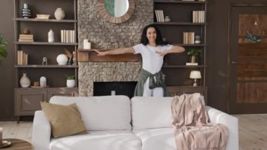 Cheerful carefree young woman moving funny listening to dynamic music cute energetic happy hispanic girl enjoying weekend at home alone active dancing dance in living room having fun laughing smiling