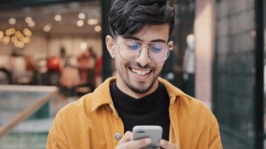Yakın plan mutlu Hintli adam akıllı telefondan komik videolar izlerken gülüyor. Sosyal ağda telefon ekranı tarama web sayfasına bakıyor. Genç adam sanal servis kullanarak arkadaşlık sitesinde mesaj yazıyor.