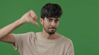 Unsatisfied man arab indian client showing thumb down negative attitude with disappointed expression show dislike disapproval bad assessment low mark gesture stand isolated in green studio chroma key