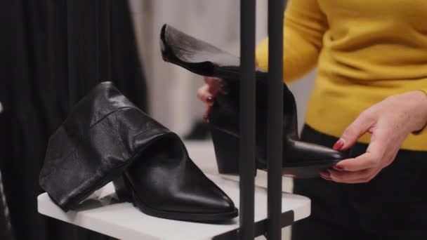 成熟的高加索女性顾客在服装店打折销售以典雅的中年女性顾客为重点的时装店精挑细选鞋看质量持有黑色女鞋 — 图库视频影像
