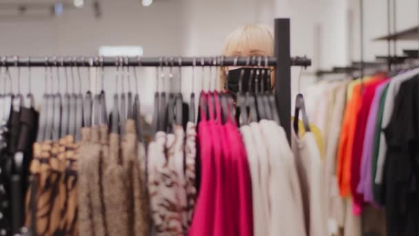 成熟的高加索女性购物者在服装店挑选服装典雅的中年女性顾客戴着保护面具在衣架上寻找合适的完美服装打折购物 — 图库视频影像
