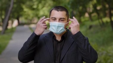 Kafkasyalı yorgun işadamı tıbbi maske takıyor koruyucu solunum cihazı takıyor. Yorgun adam parkta duruyor. Özgürlüğü hissediyor.