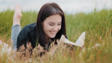 Young attractive brunette caucasian woman girl lying on grass pretty teenage girlfriend student read interesting book educational literature novel bestseller enjoy history in textbook turn over pages
