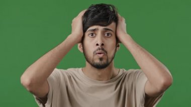 Close-up male portrait shocked upset arabian man holding hands on head failure reaction hear horror sad bad news feeling unpleasantly surprised frightened scared hispanic guy standing in green studio