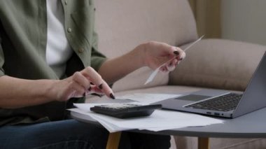Close up female old hands of senior woman housewife businesswoman holding check account counting on calculator money planning budget financial loan pay with online app in laptop managing bank finances
