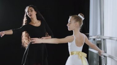 Adult woman dancer dance teacher coach tells teenage girl ballerina advice helps move gracefully with hands near ballet barre at lesson dancing feminine movements rehearsal preparation for performance