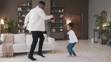 Oturma odasında dans eden Afrikalı aile taşınma gününü kutluyor. Amerikan melez babası ve kız çocuğu zıplayan kız bacaklarını hareket ettiriyor müzik eşliğinde dans ediyor baba ve kız öğrenci hobisinin keyfini çıkarıyor.