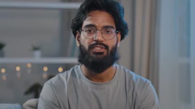 Yetişkin sakallı Hintli Arap adam, gözlüklü, vlogger blogcu, kameralı, canlı görüntülü konferans, konuşma, uzaktan sohbet, blog vlog, ev kamerasının önündeki kanepede otur.