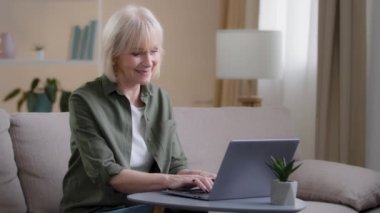 Yaşlı bir kadın, ev ofisteki koltukta oturmuş, dizüstü bilgisayarda yaşlı bir bayanla çalışıyor ve web sitesinde e-posta yazıp başvuru formu dolduruyor. Olgun kadın bilgisayar sohbeti çevrimiçi ödeme alışveriş uygulaması