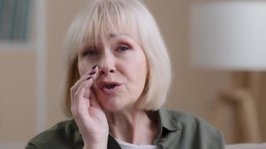 Portrait at home old Caucasian grandmother close mouth with hand whispering telling secret senior grandma 60s woman gossiping talking confidential information whisper say secrecy mystery trust concept