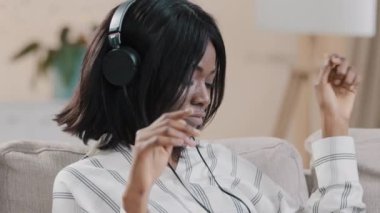 Yakın plan genç kaygısız kadın kanepede oturup kulaklıkla ritmik müzik dinliyor favori müzik parçasının keyfini çıkarıyor eğlenceli kız hafta sonu dinamik dansı yapıyor rahatlıyor.
