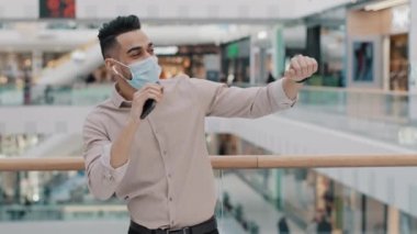 Arap İspanyol erkek işadamı tıbbi maske takan Arap bir adam şirket alışveriş merkezinde mobil ses uygulaması ile dans ediyor müzik eşliğinde dans ediyor neşeli bir zafer kazanıyor.