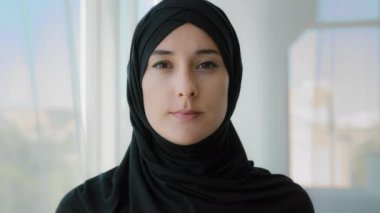 Portre, Arap Müslüman, siyah başörtüsü takmış, klasik başörtüsü takmış, kusursuz ciltli, sakin bir kız portresi. Siyah başörtüsü takan kadın yüzü evde kameraya bakıyor.