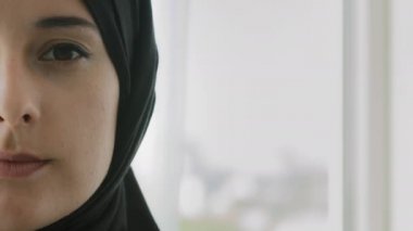 Close up half female face of Muslim woman in black hijab indoors. Portrait Islamic Arabian girl with natural make up skin care anti acne remedy. Headshot of serene lady in headscarf looking at camera