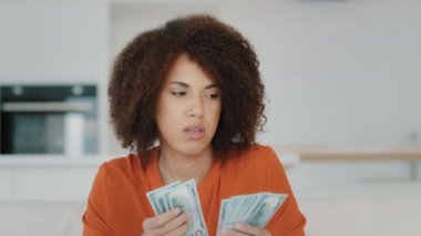 Thoughtful pensive wealthy African American businesswoman counting dollar salary credit from bank cash thinks about finance spending at home biracial girl with curly hair counts money financial saving