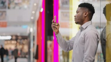 Young male blogger holding phone taking pictures using mobile application focused serious guy looks at smartphone screen checking email browsing social network makes order in online store on telephone