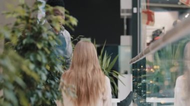 Friendly smiling young male waiter in apron serves client girl in cafe affable restaurant worker barman brings coffee drink in paper cup customer in cafeteria communicates with visitor accepts order