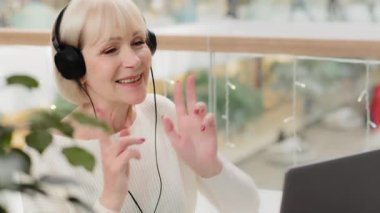 Kulaklıklı müzik dinleyen olgun, neşeli, neşeli, orta yaşlı bir büyükanne torunlarıyla online konferansta eğlenirken video aracılığıyla iletişim kuruyor.
